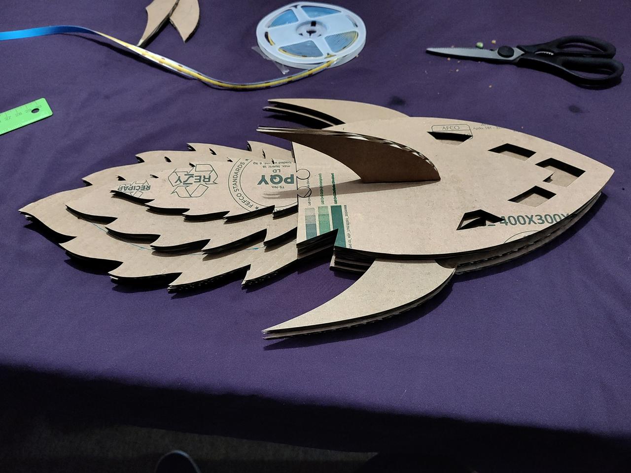 Cardboard mockup of the main panels, stacked to show how the pieces stack. There is a reel of COB LED strip, and a pair of kitchen scissorsin the background.